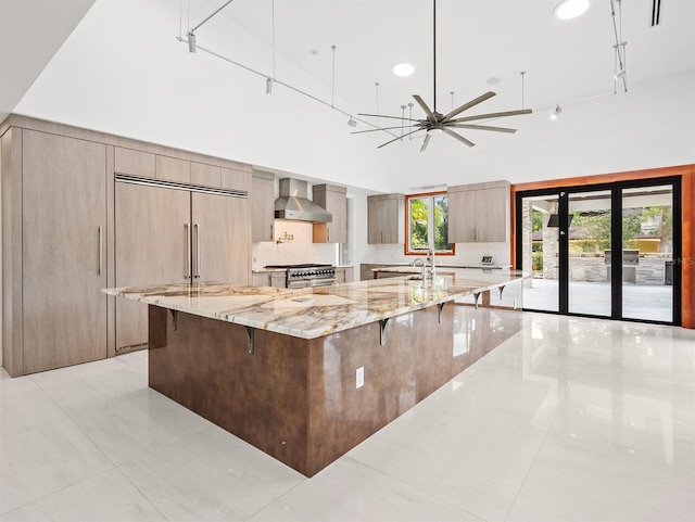 kitchen with tasteful backsplash, light stone counters, a breakfast bar, a spacious island, and wall chimney range hood