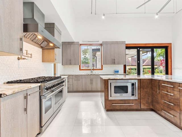 kitchen featuring decorative backsplash, light stone counters, wall chimney range hood, and appliances with stainless steel finishes