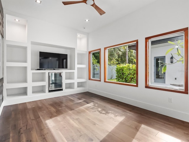 unfurnished living room featuring built in shelves, hardwood / wood-style flooring, beverage cooler, and ceiling fan