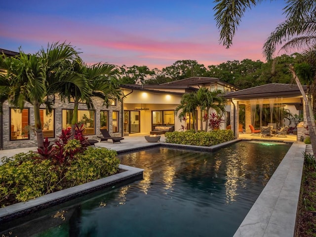 pool at dusk with outdoor lounge area and a patio