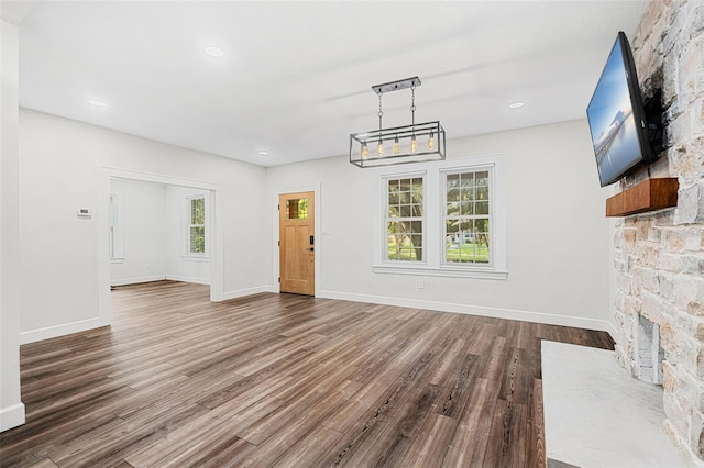 unfurnished living room featuring a stone fireplace and dark hardwood / wood-style flooring