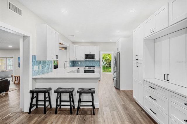 kitchen featuring stainless steel appliances, kitchen peninsula, wood-type flooring, a kitchen bar, and white cabinets