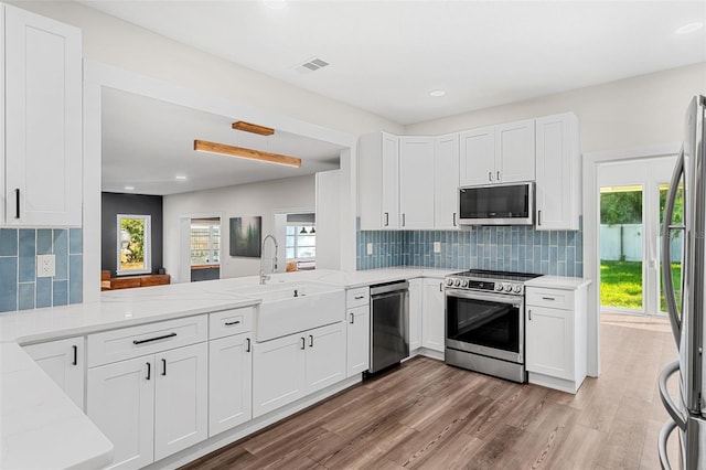 kitchen featuring white cabinets, sink, appliances with stainless steel finishes, tasteful backsplash, and kitchen peninsula