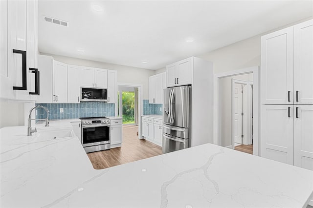 kitchen featuring light stone countertops, sink, decorative backsplash, white cabinets, and appliances with stainless steel finishes