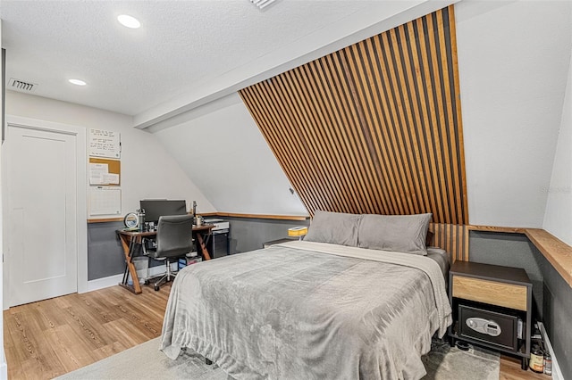 bedroom with a textured ceiling, light hardwood / wood-style flooring, and vaulted ceiling