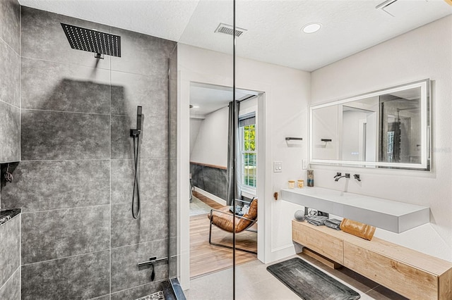 bathroom with tile patterned floors, vanity, a textured ceiling, and tiled shower