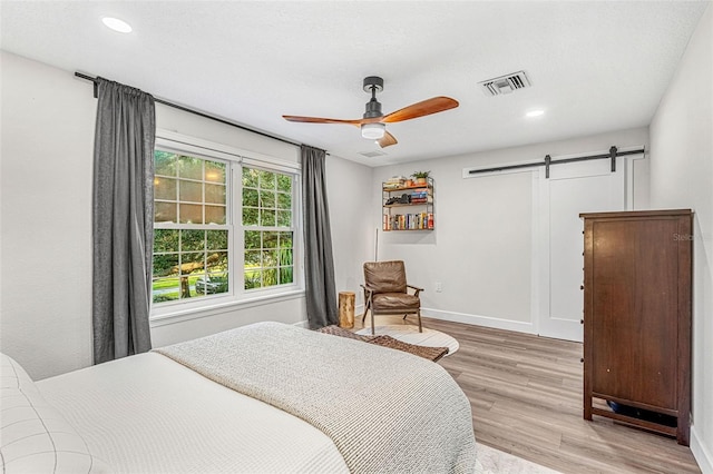 bedroom featuring light wood-type flooring, a barn door, and ceiling fan