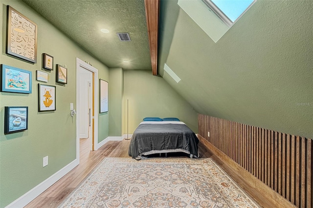 bedroom with vaulted ceiling with skylight, light wood-type flooring, and a textured ceiling