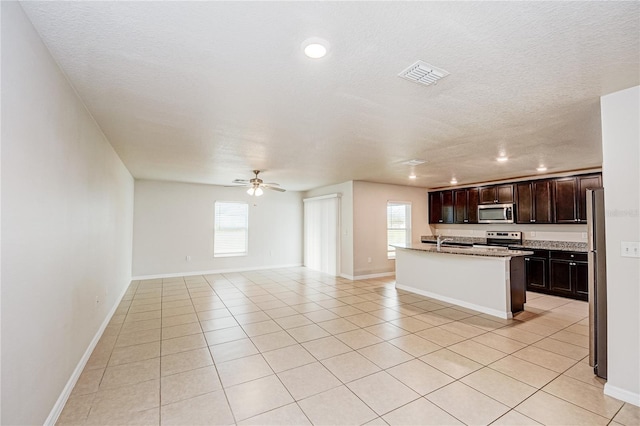 kitchen featuring ceiling fan, appliances with stainless steel finishes, dark brown cabinets, an island with sink, and light tile patterned flooring