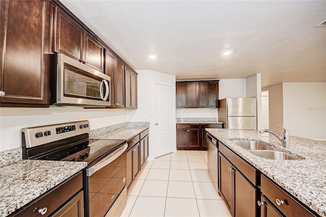 kitchen with appliances with stainless steel finishes, sink, light tile patterned floors, dark brown cabinetry, and light stone counters