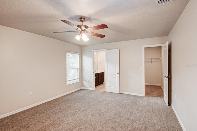 unfurnished bedroom featuring a walk in closet, ensuite bath, a textured ceiling, a closet, and light colored carpet