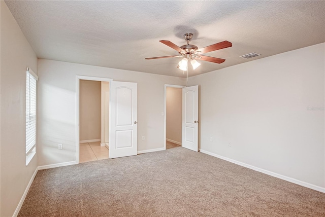 unfurnished bedroom with ceiling fan, light colored carpet, and a textured ceiling