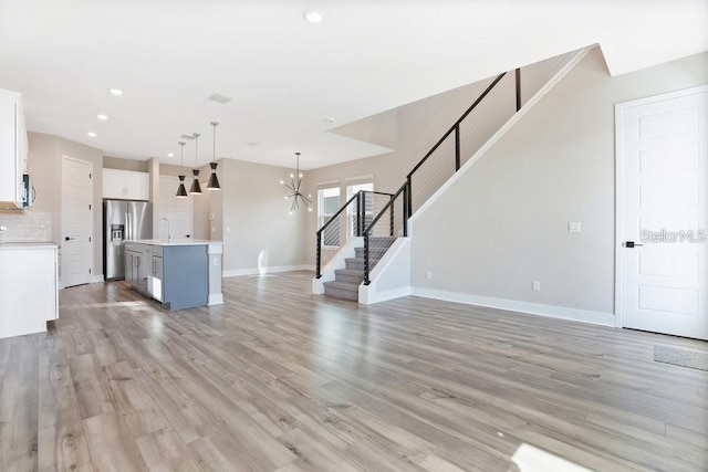 unfurnished living room with a notable chandelier, light wood-type flooring, and sink