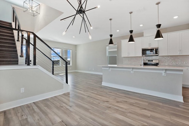 kitchen with a kitchen breakfast bar, hanging light fixtures, appliances with stainless steel finishes, white cabinetry, and a chandelier