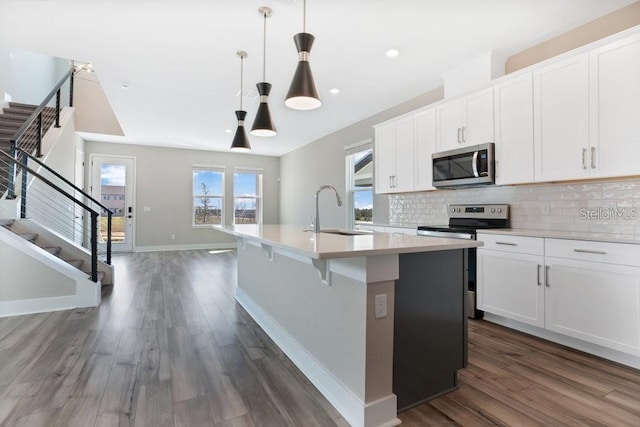 kitchen with pendant lighting, a center island with sink, white cabinets, sink, and appliances with stainless steel finishes