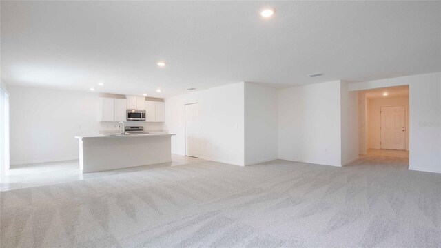 unfurnished living room featuring light carpet and sink