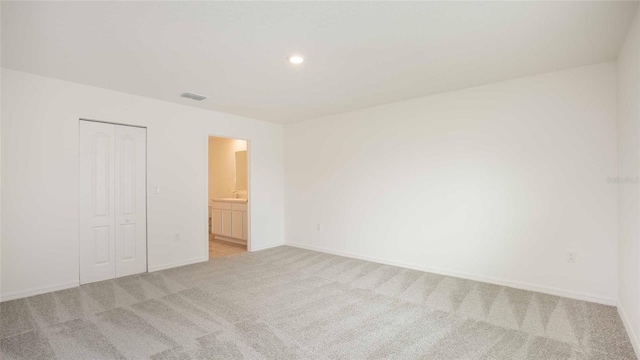 unfurnished bedroom with ensuite bathroom, a closet, and light colored carpet