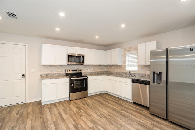 kitchen with appliances with stainless steel finishes, light wood-type flooring, light stone countertops, white cabinets, and sink