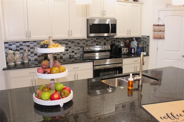 kitchen with stainless steel appliances, sink, white cabinetry, dark stone countertops, and backsplash