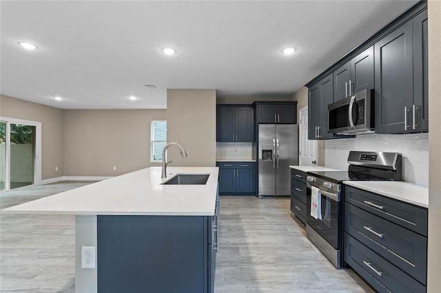 kitchen with decorative backsplash, light wood-type flooring, stainless steel appliances, sink, and an island with sink