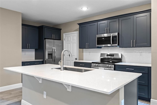 kitchen with a kitchen island with sink, sink, decorative backsplash, light hardwood / wood-style floors, and stainless steel appliances