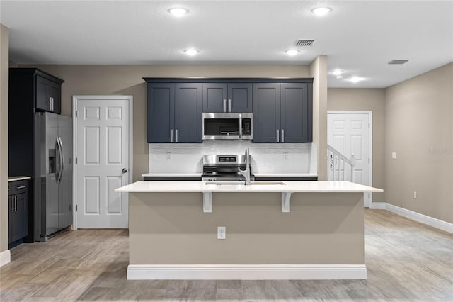 kitchen featuring a center island with sink, sink, light hardwood / wood-style flooring, tasteful backsplash, and stainless steel appliances