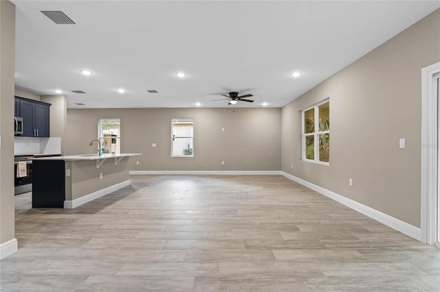 unfurnished living room with ceiling fan, light wood-type flooring, and sink