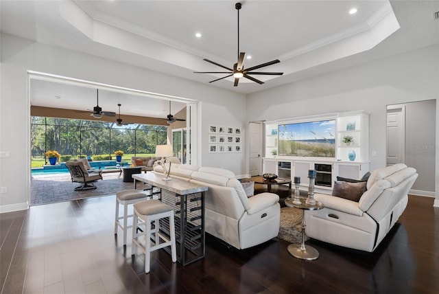 living room featuring ornamental molding, a tray ceiling, a wealth of natural light, and dark wood-type flooring