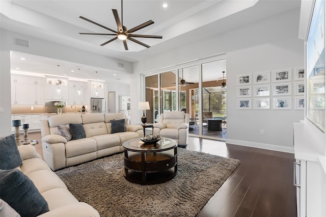 living room with a high ceiling, a raised ceiling, crown molding, dark hardwood / wood-style floors, and ceiling fan