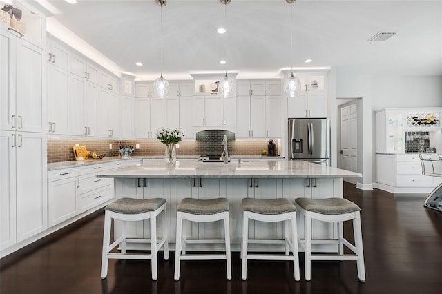 kitchen with stainless steel fridge with ice dispenser, decorative light fixtures, white cabinetry, and a kitchen island with sink