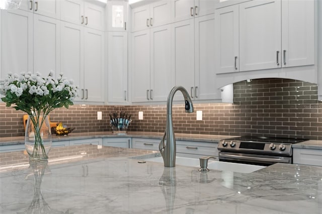 kitchen with white cabinets, decorative backsplash, light stone countertops, and high end stainless steel range