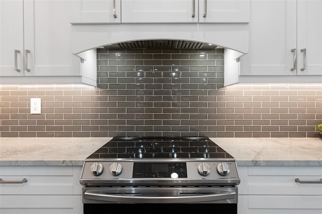 kitchen with light stone countertops, backsplash, white cabinetry, and stainless steel range oven