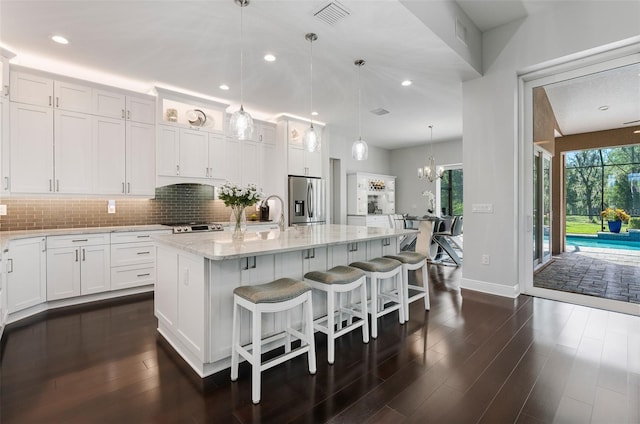 kitchen featuring dark wood-type flooring, hanging light fixtures, stainless steel fridge, a center island with sink, and white cabinets