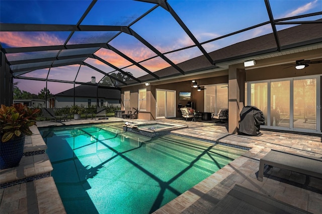 pool at dusk featuring ceiling fan, a patio area, a lanai, and an in ground hot tub