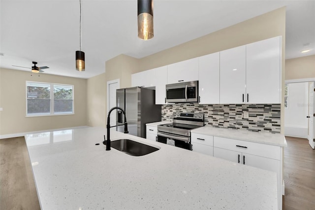 kitchen with backsplash, stainless steel appliances, light stone countertops, white cabinets, and decorative light fixtures