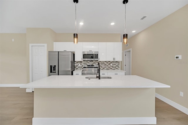 kitchen with pendant lighting, stainless steel appliances, a center island with sink, and white cabinets