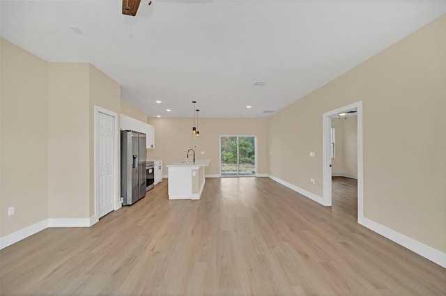 unfurnished living room with ceiling fan, sink, and light wood-type flooring