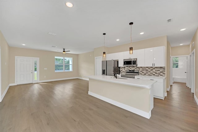 kitchen featuring decorative light fixtures, an island with sink, white cabinetry, stainless steel appliances, and plenty of natural light