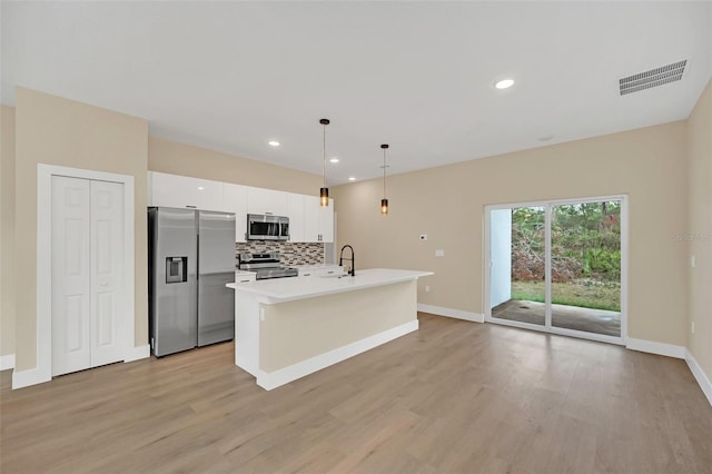 kitchen with appliances with stainless steel finishes, pendant lighting, an island with sink, white cabinets, and decorative backsplash