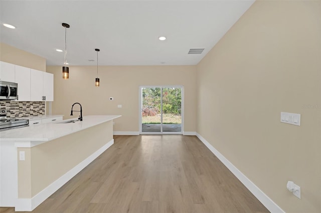 kitchen featuring pendant lighting, tasteful backsplash, sink, stainless steel appliances, and light wood-type flooring