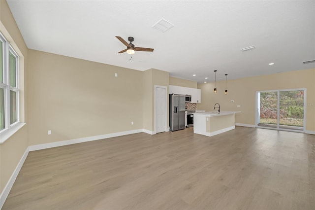 unfurnished living room featuring ceiling fan, sink, and light wood-type flooring