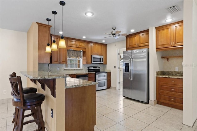 kitchen with stone counters, hanging light fixtures, stainless steel appliances, a kitchen breakfast bar, and kitchen peninsula