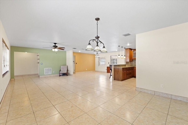 unfurnished living room with light tile patterned flooring, a healthy amount of sunlight, and ceiling fan with notable chandelier