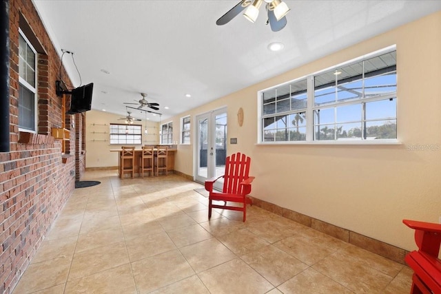 sitting room featuring ceiling fan, light tile patterned flooring, brick wall, and french doors