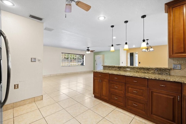 kitchen with light stone countertops, pendant lighting, ceiling fan with notable chandelier, and a textured ceiling