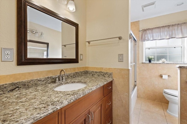 full bathroom with bath / shower combo with glass door, vanity, tile walls, tile patterned flooring, and toilet