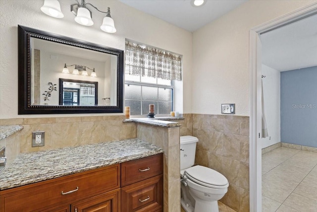 bathroom with toilet, vanity, tile patterned floors, and tile walls