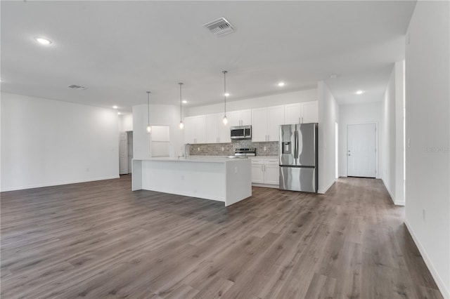 kitchen featuring appliances with stainless steel finishes, white cabinets, dark hardwood / wood-style floors, hanging light fixtures, and an island with sink