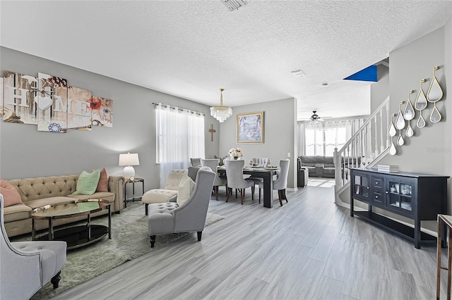 living room featuring ceiling fan with notable chandelier, a textured ceiling, and light hardwood / wood-style flooring