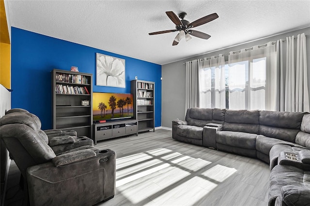 living room with ceiling fan, a textured ceiling, and light wood-type flooring